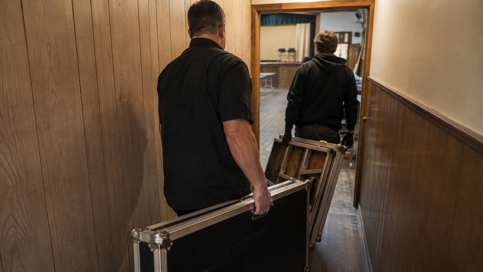 Event booth equipment being carried through a narrow corridor into an older hall