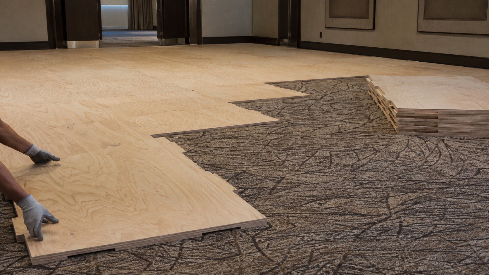 Level plywood base being laid over carpet before a vinyl dance floor goes down