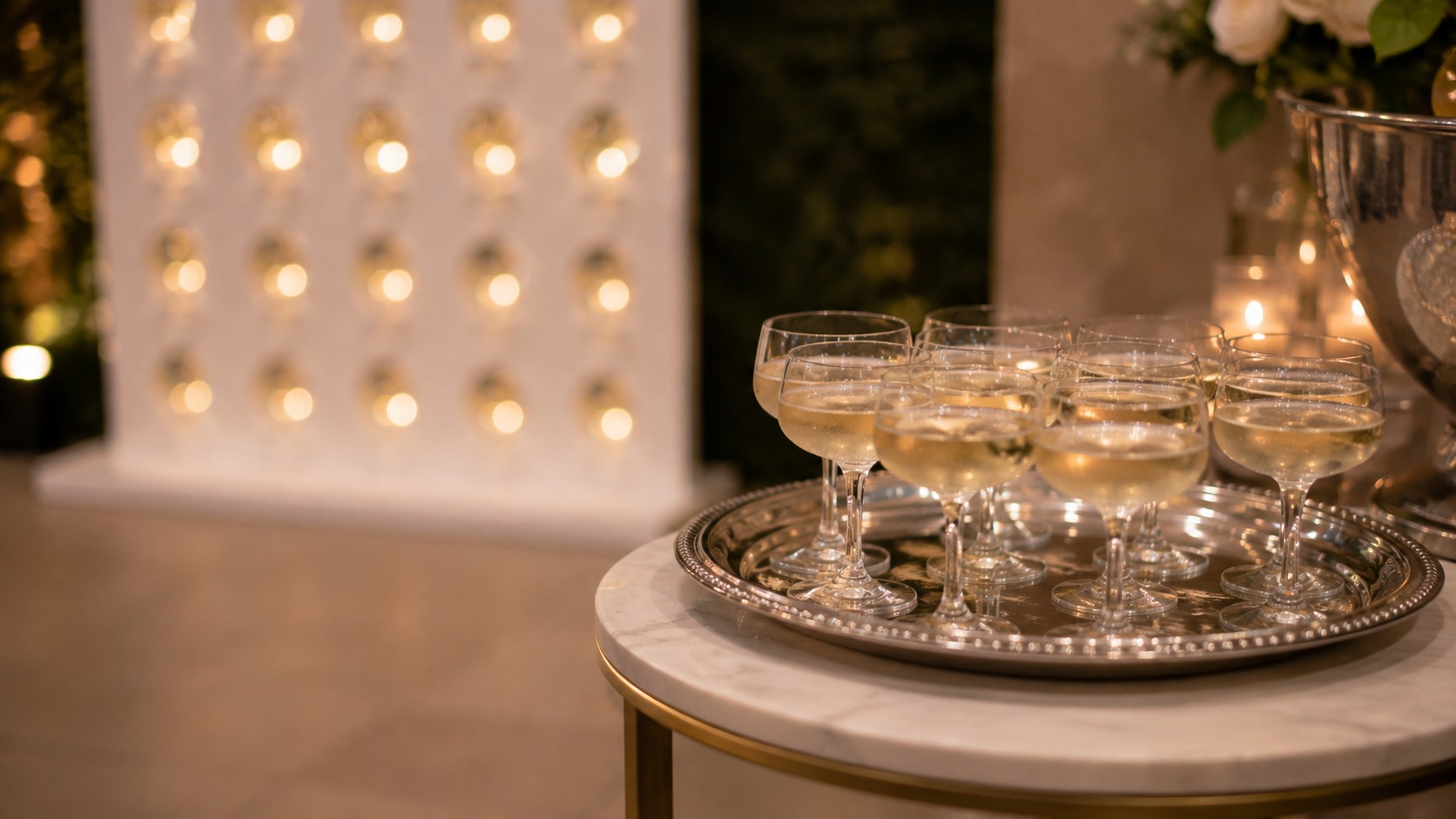 Tray of pre poured glasses waiting on a side table beside a champagne wall